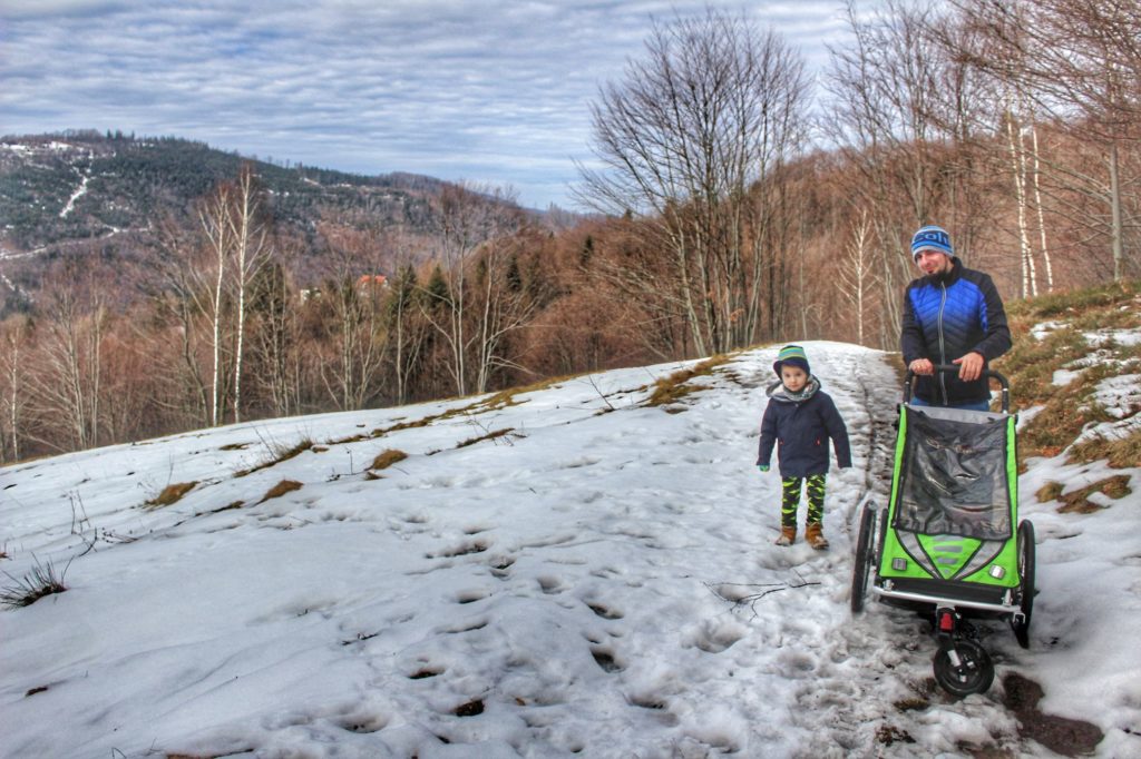 Turysta z wózkiem i dzieckiem idący przez zaśnieżoną polanę w Brennej