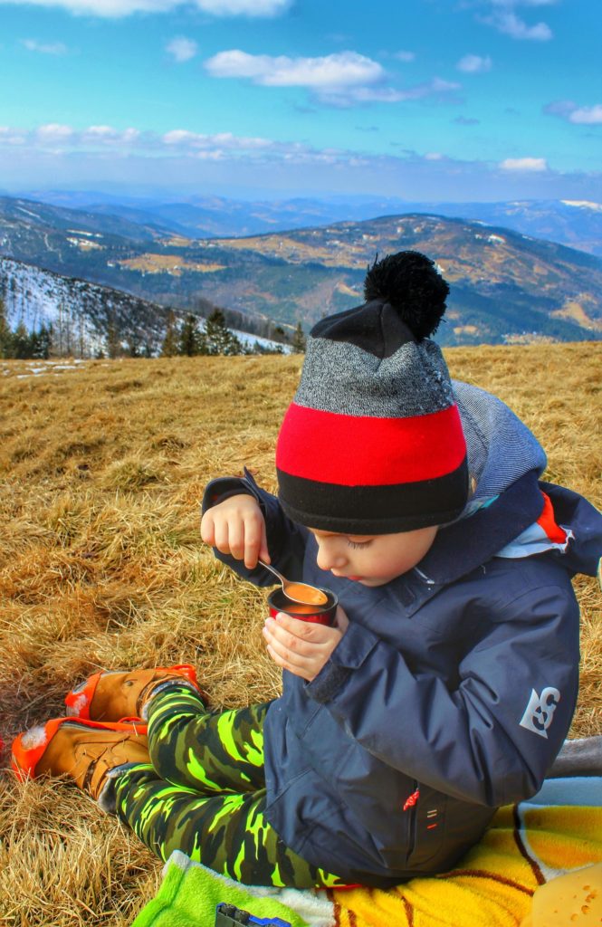 Dziecko na Hali Pawlusiej jedzące zupę pomidorową, siedzące na kocu, w tle krajobraz górski