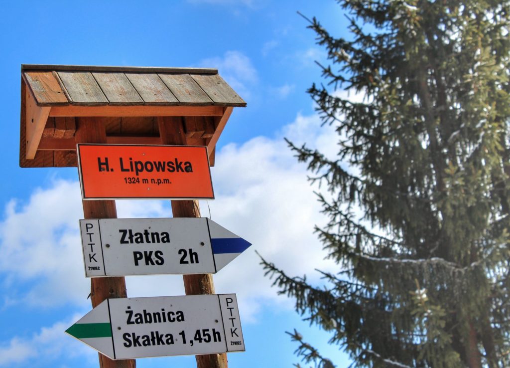 Pomarańczowa tabliczka z napisem H. Lipowska 1324 m n.p.m. drogowskazy szlak niebieski Złatna PKS 2h oraz szlak zielony Żabnica Skałka 1,45h