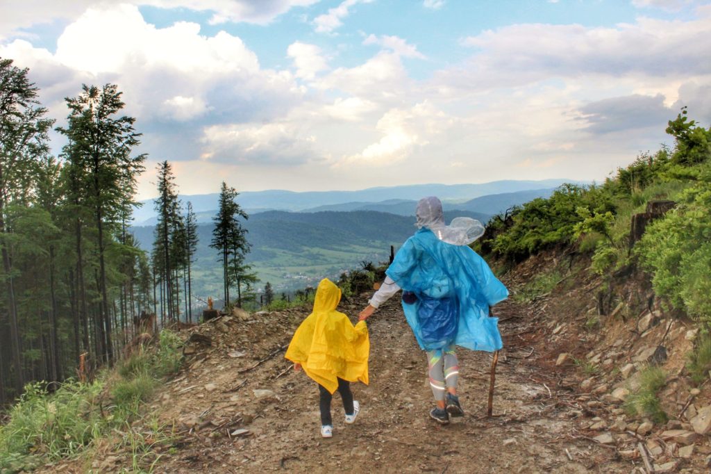 Turystka z dzieckiem idąca drogą pożarową, w oddali krajobraz górski, deszczowy dzień