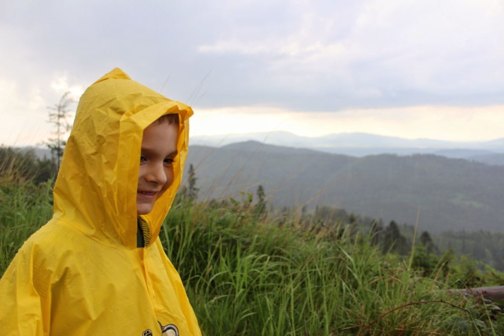 Uśmiechnięte dziecko na szlaku na niebieskim szlaku Romankę, dziecko ubrane w żółtą pelerynę przeciwdeszczową, krajobraz górski
