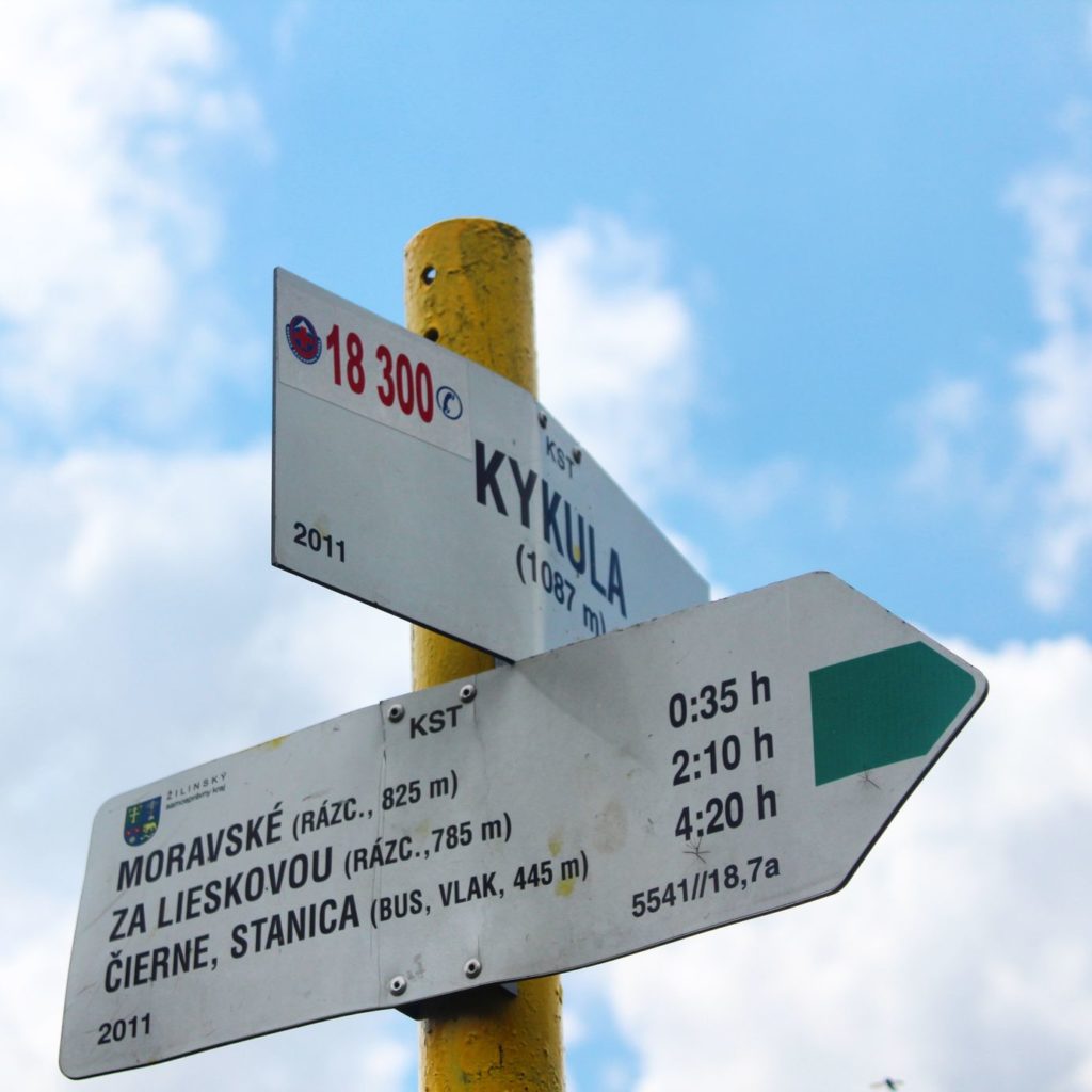słup z tabliczką oznaczającą słowacki szczyt Kikula leżący 1087 metrów nad poziomem morza oraz opis zielonego szlaku prowadzącego ze szczytu