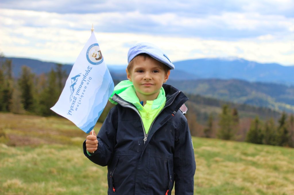 Jałowiec z dzieckiem, chłopiec trzymający flagę akcji Zdobywamy Szczyty dla Hospicjum, w tle krajobraz górski
