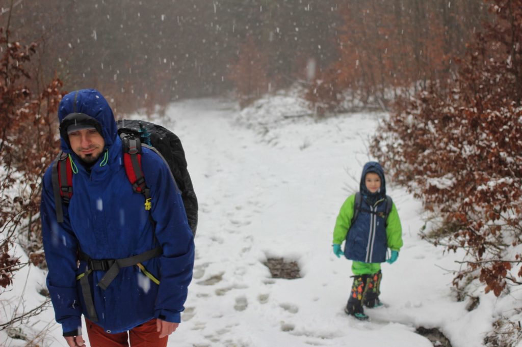 Turysta z dzieckiem idący leśną ścieżką, jesień, padający śnieg