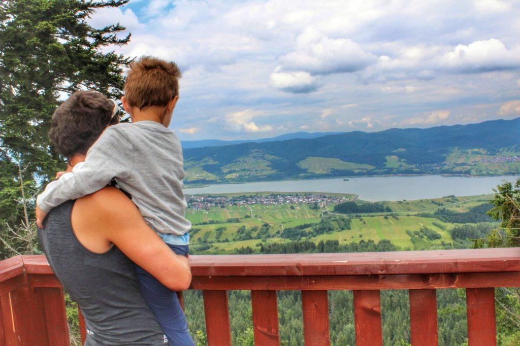 Turysta z dzieckiem na rękach na wieży widokowej Żar w Pieninach Spiskich, widok między innymi na Jezioro Czorsztyńskie
