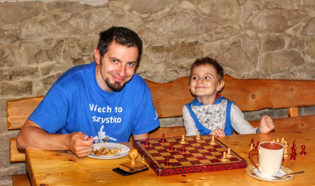Turysta z dzieckiem w Schronisku Górskim W Murowanej Piwnicy jedzący szarlotkę i grający w szachy