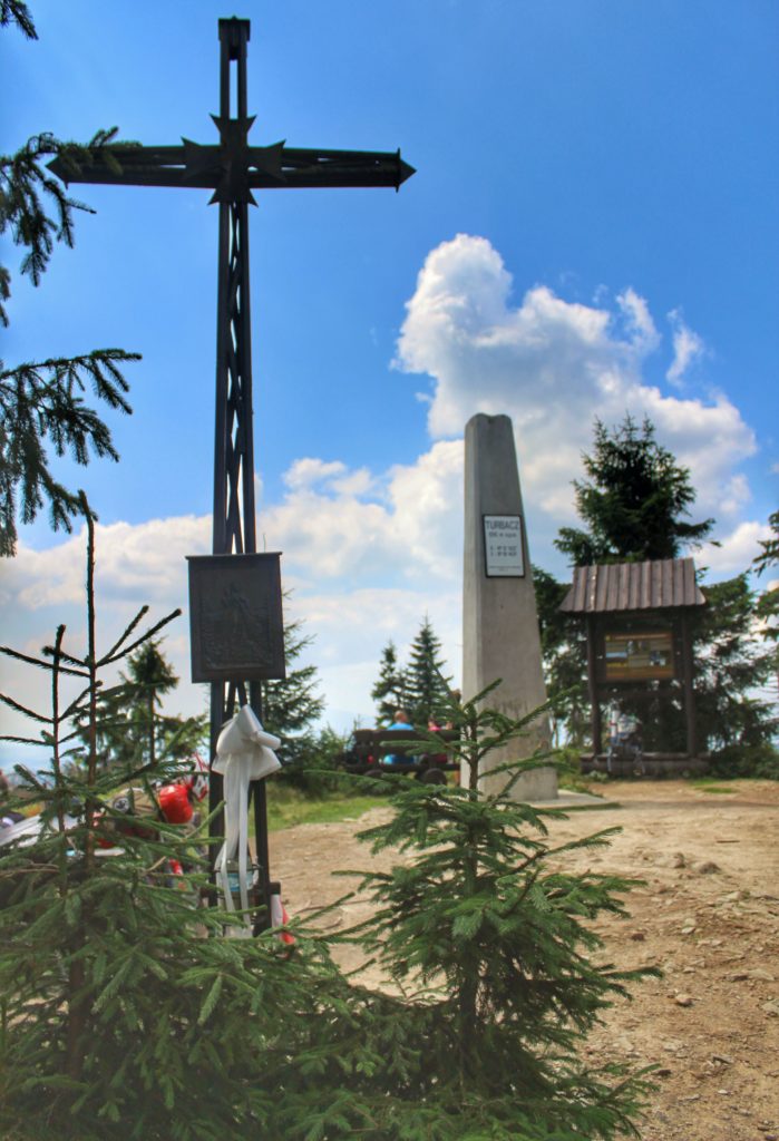 Krzyż na Turbaczu, w oddali widoczny betonowy pomnik z białą tablicą