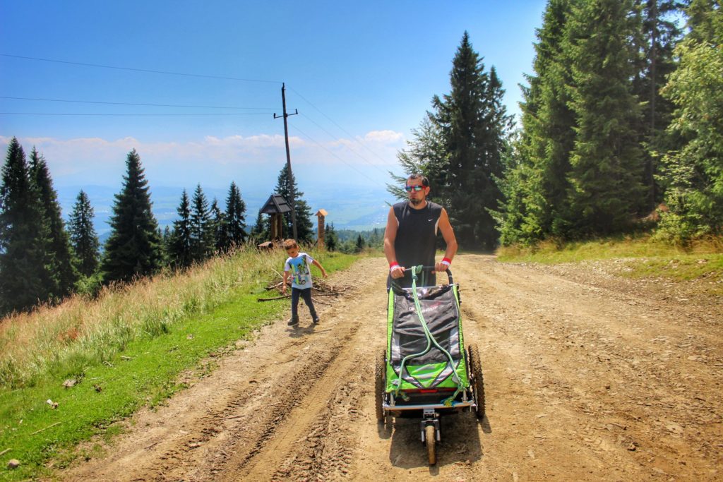 Turysta pchający wózek, dziecko idące obok, szeroka droga prowadząca na Turbacz