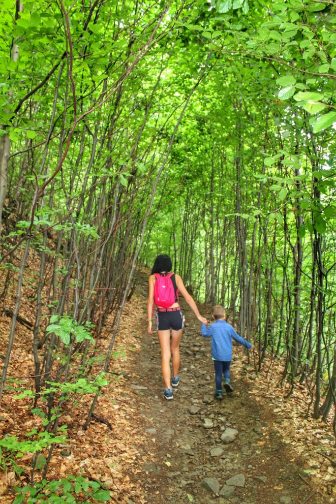 Turystka idąca z dzieckiem leśną ścieżką, letnia pora