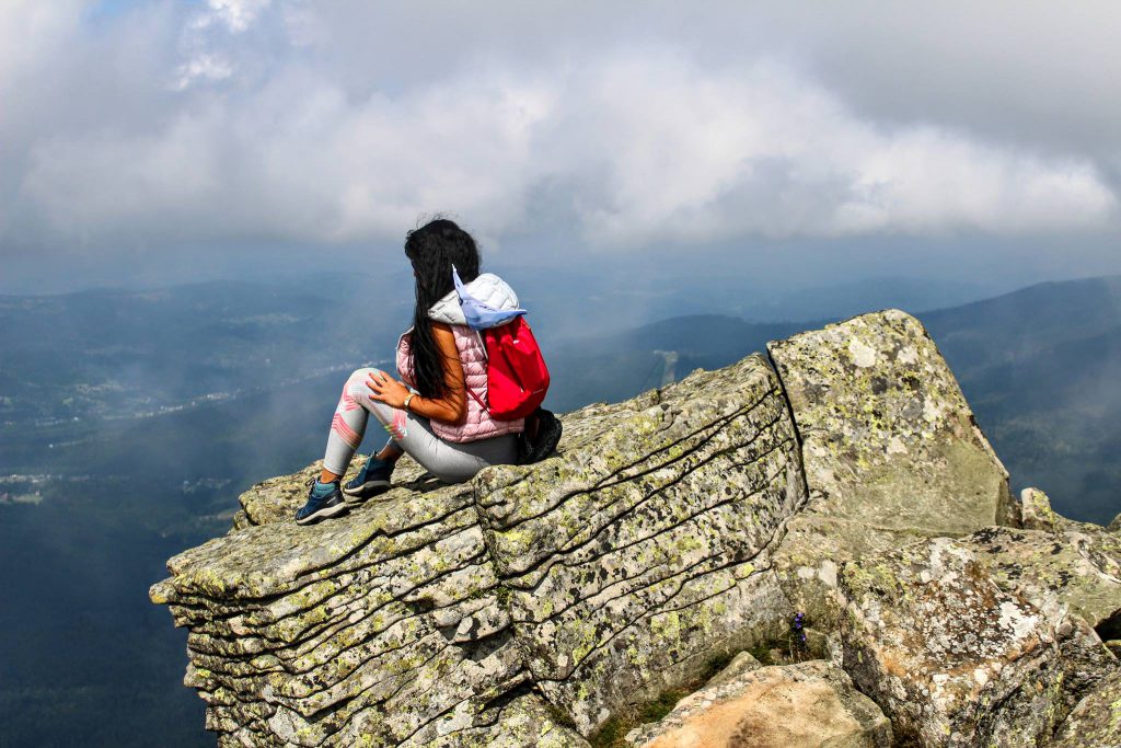 Kobieta siedząca na skale na tle zamglonych widoków górskich, niebo pełne gęstych chmur