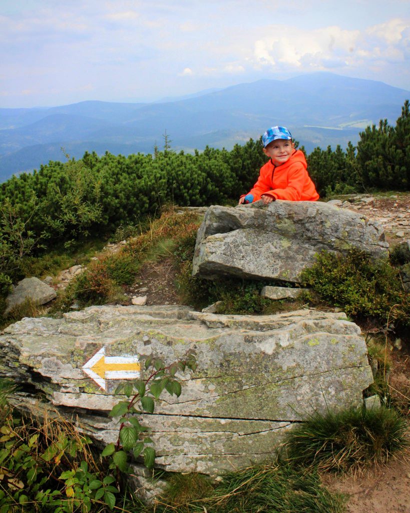 Uśmiechnięte dziecko siedzące na skałach, oznaczenie żółtego szlaku prowadzącego ze szczytu Pilsko do Schroniska na Hali Miziowej 