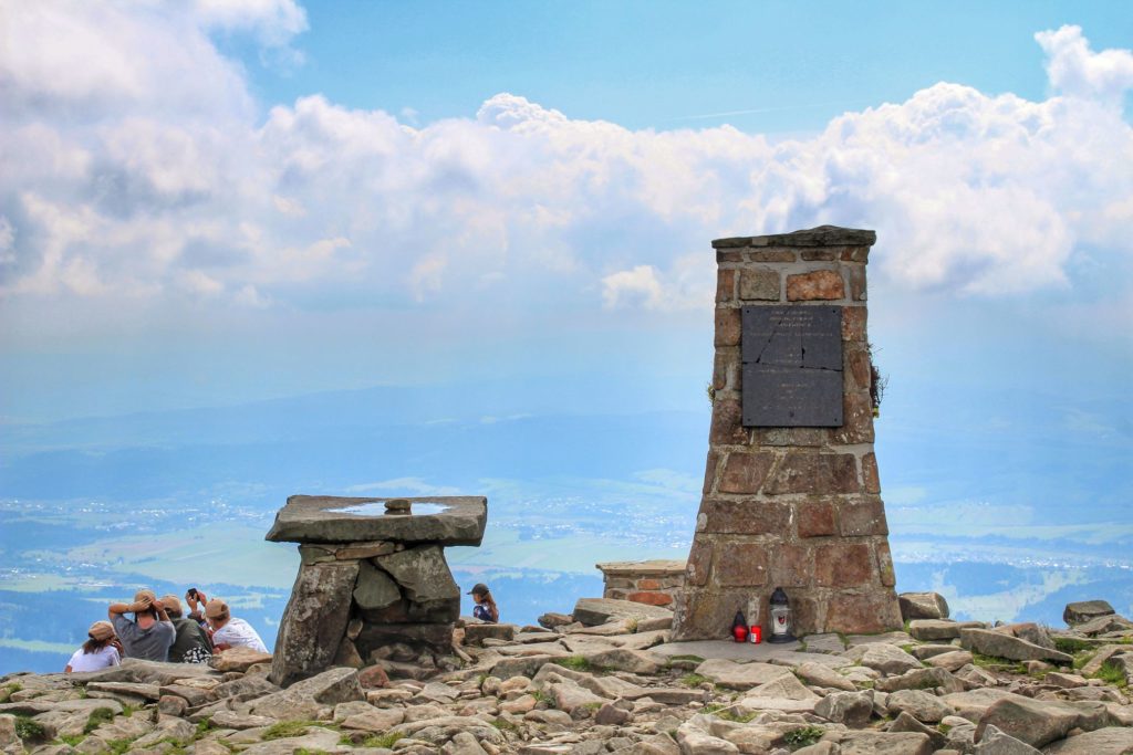 Pomnik na Babiej Górze, grupka turystów robiąca sobie zdjęcie, skały, chmury