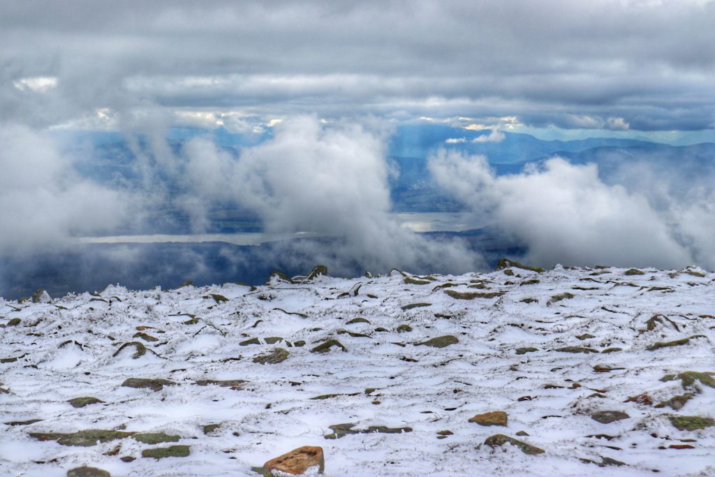 widok na jezioro Orawskie z Babiej Góry wyłaniający się zza chmur, ośnieżone kamienie