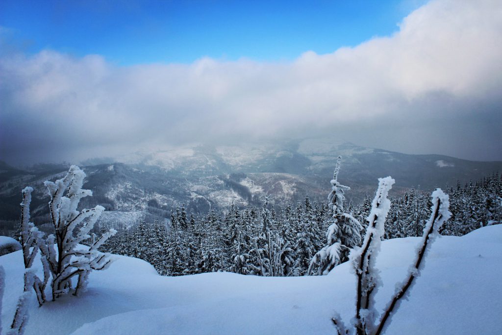 Magurka Radziechowska zimą, ośnieżona wychodnia skalna, widok na okoliczne szczyty zakryte częściowo przez gęste chmury 