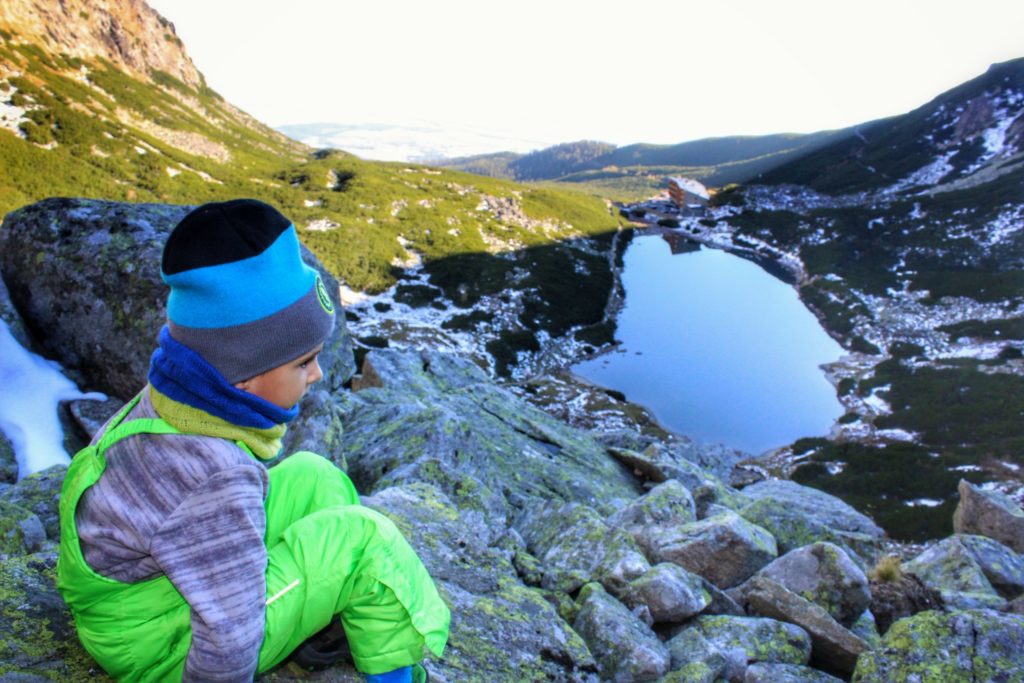 Czteroletnie dziecko siedząca na skałach w Tatrach Wysokich obserwujące z góry Wielicki Staw oraz Hotel Górski - Dom Śląski