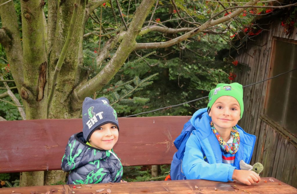 Dzieci odpoczywające przy drewnianym stole na żółtym szlaku z Wisły na Trzy Kopce Wiślańskie, w tle drzewo, na której jest pomarańczowa jarzębina