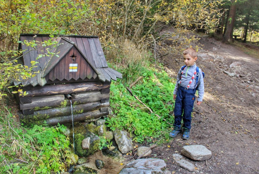 Dziecko przy drewnianym domku, z którego wylatuje górska woda, szlak żółty w Tatrach Wysokich na Słowacji