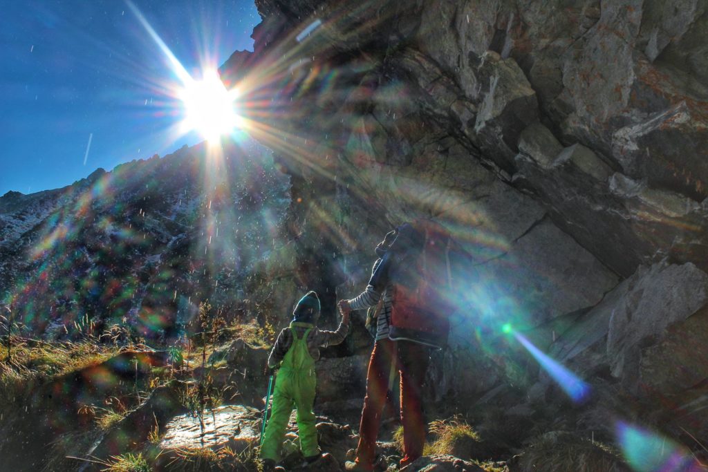 Turysta z dzieckiem idący kamienistym szlakiem pod skałami, z których kapie woda, na niebie pełne słońce, Dolina Wielicka