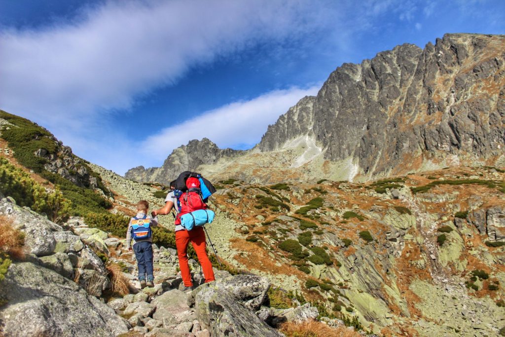 Turysta z dzieckiem idący po skałach w kierunku Batyżowieckiego Stawu, po prawej stronie szczyt Gerlach