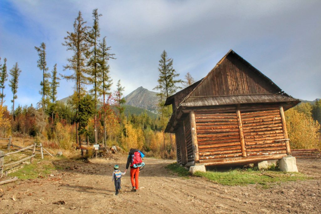 Turysta z dzieckiem maszerujący żółtym szlakiem prowadzącym z Wyżnie Hagi, po prawej stronie drewniana chata 