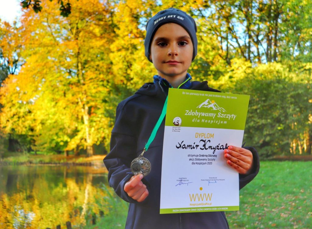Dziecko trzymające dyplom oraz medal zdobyty w akcji zdobywamy szczyty dla hospicjum, jesienny park w Pszczynie