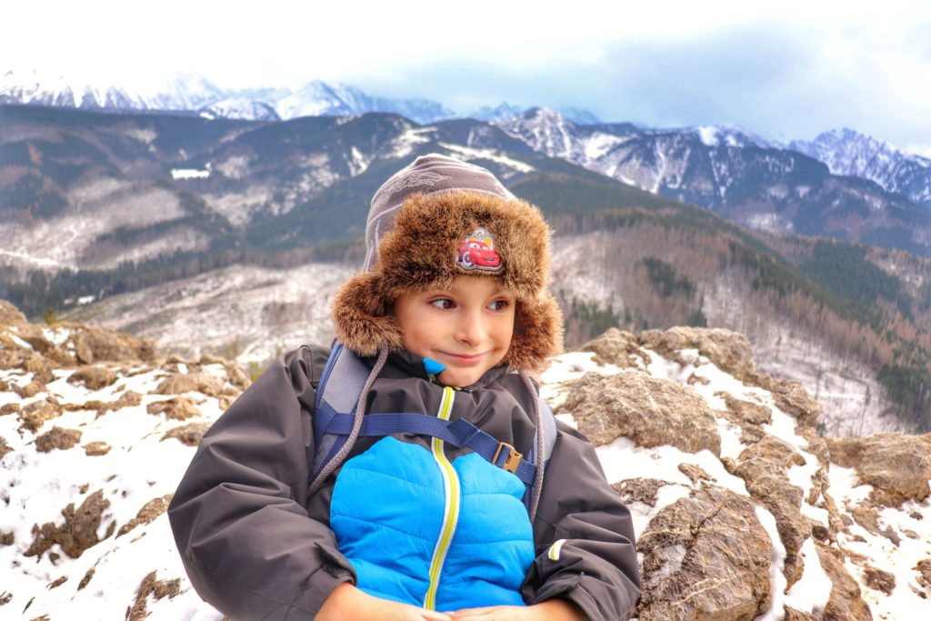 Szczęśliwe dziecko siedzące na skałach na wierzchołku szczytu Nosal, w tle Tatry w zimowej odsłonie