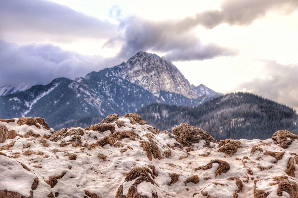 Szczyt Nosal zimą, skały pokryte śniegiem, w tle tatrzańskie szczyty, zachmurzone niebo