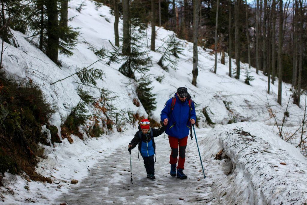 Dziecko idące z tatą oblodzoną, dość szeroką drogą, w koło zalega śnieg