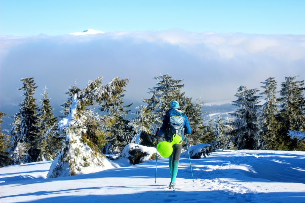 Turystka stojąca tyłem z kijkami trekingowymi w zaśnieżonym terenie, w tle morze mgieł oraz wierzchołek Babiej Góry 