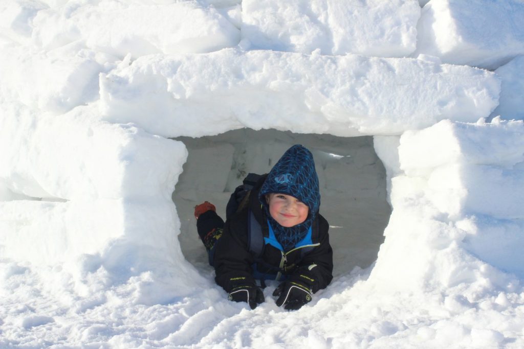 Uśmiechnięte dziecko leżące w śnieżnym igloo 