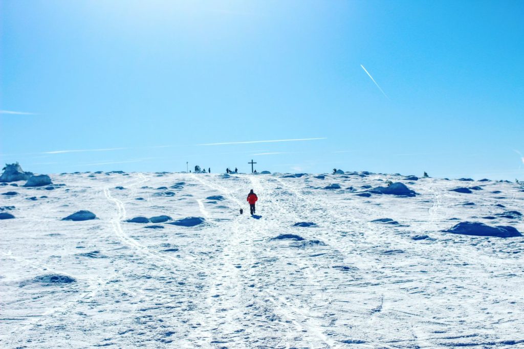 Turysta idący po zaśnieżonym terenie w kierunku szczytu Pilsko, w tle widoczny krzyż na Pilsku 
