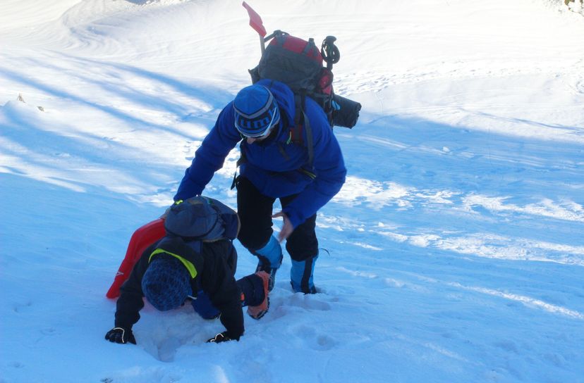 Mężczyzna asekurujący dziecko wychodzące na czworaka pod zaśnieżoną górę