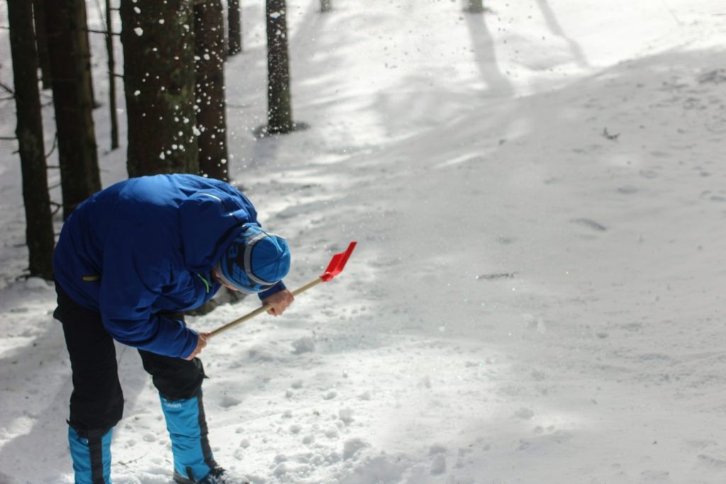Mężczyzna odgarniający śnieg czerwoną łopatą 