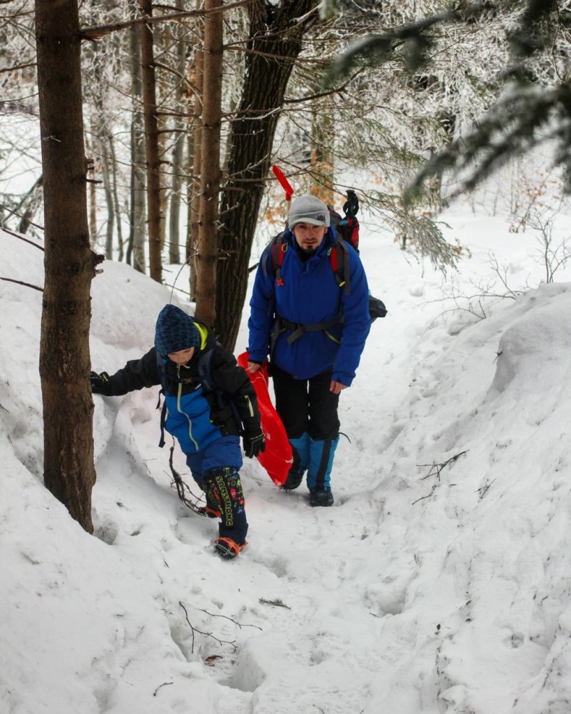 Dziecko idące z ojcem stromo w górę po zaśnieżonym terenie w lesie