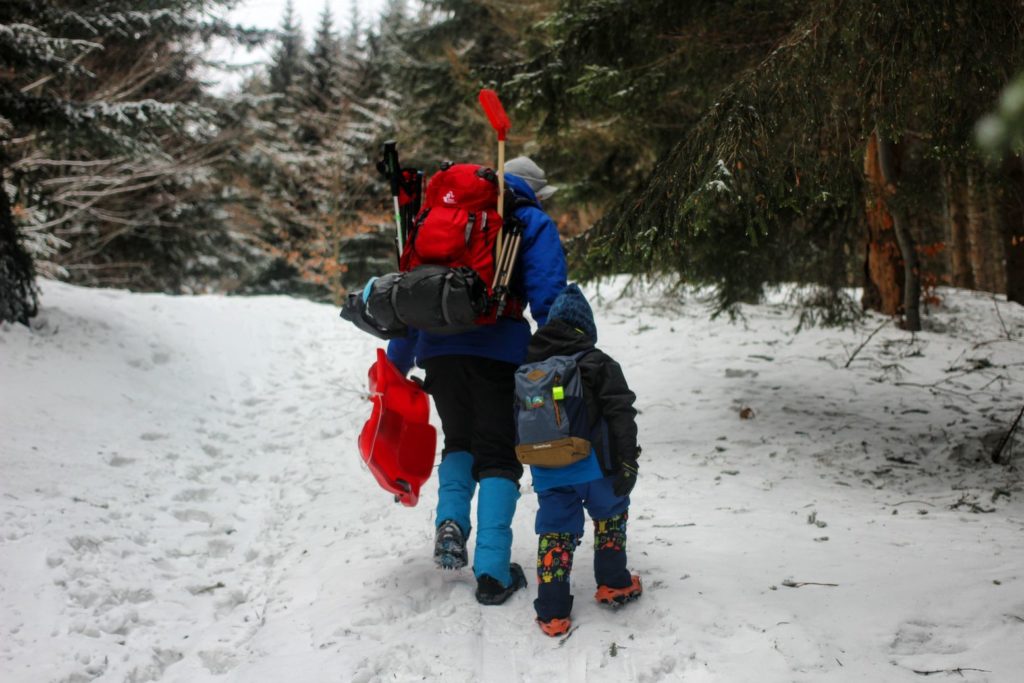 Mężczyzna z dzieckiem idący po śniegu, załadowany plecak turystyczny 