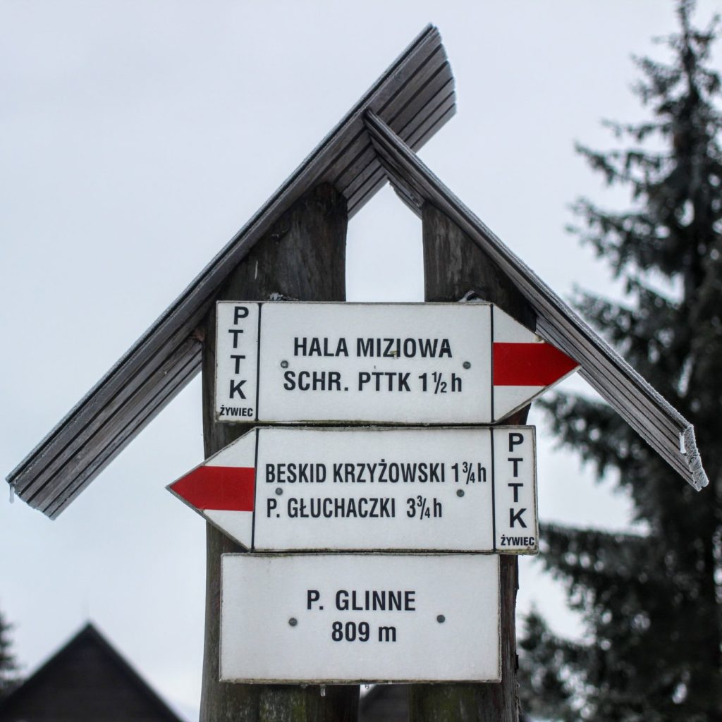 Biała tablica oznaczająca Przełęcz Glinne oraz drogowskaz opisujący szlak czerwony