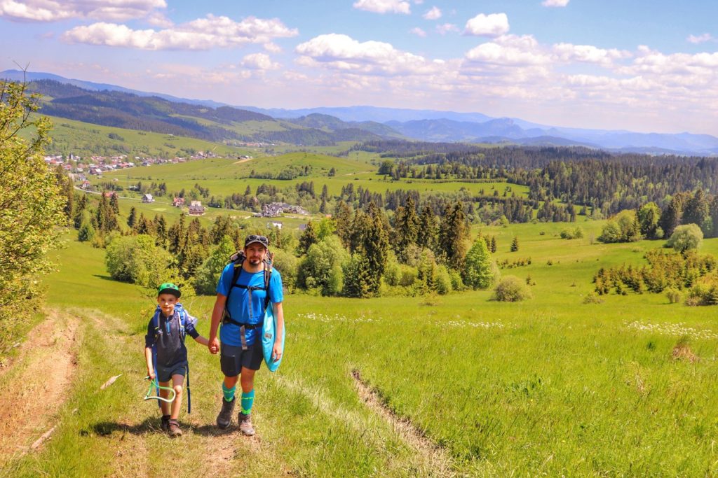 Turysta z dzieckiem, Łapsze Wyżne szlak czerwony, obszerna polana w Pieninach Spiskich, wiosenne kolory, w tle krajobraz górski