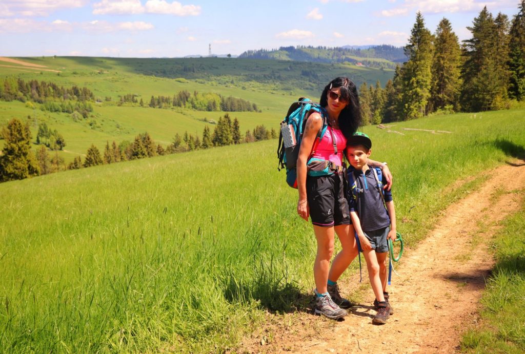 Turystka z dzieckiem na czerwonym szlaku na Rzepiska, w tle szczyt Grandeus, polana