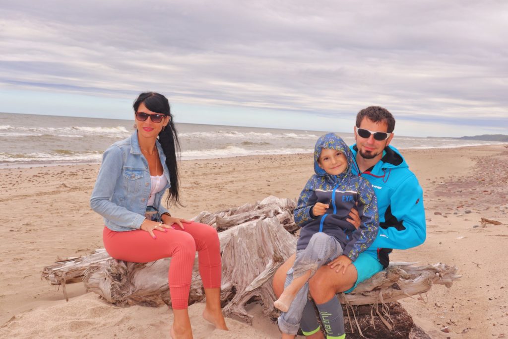 Trzyosobowa, szczęśliwa rodzina, dziecko siedzące na kolanach taty, plaża w Orzechowie