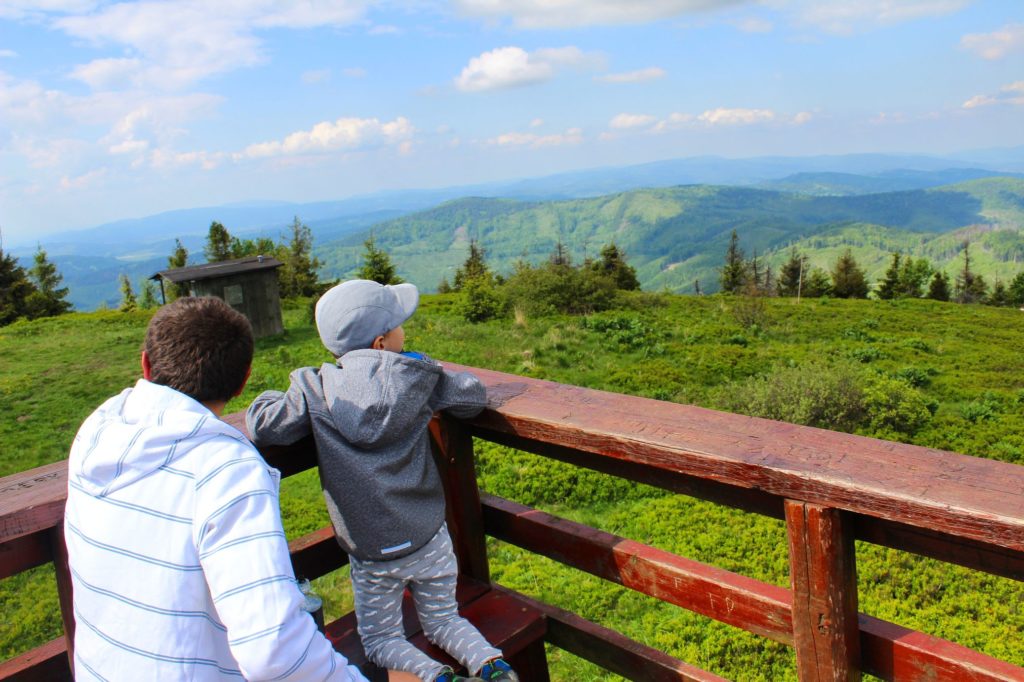 Mężczyzna z dzieckiem na platformie widokowej na Wielkiej Raczy patrzący w kierunku Beskidy Żywieckiego, niebieskie niebo z białymi obłokami, krajobraz górski