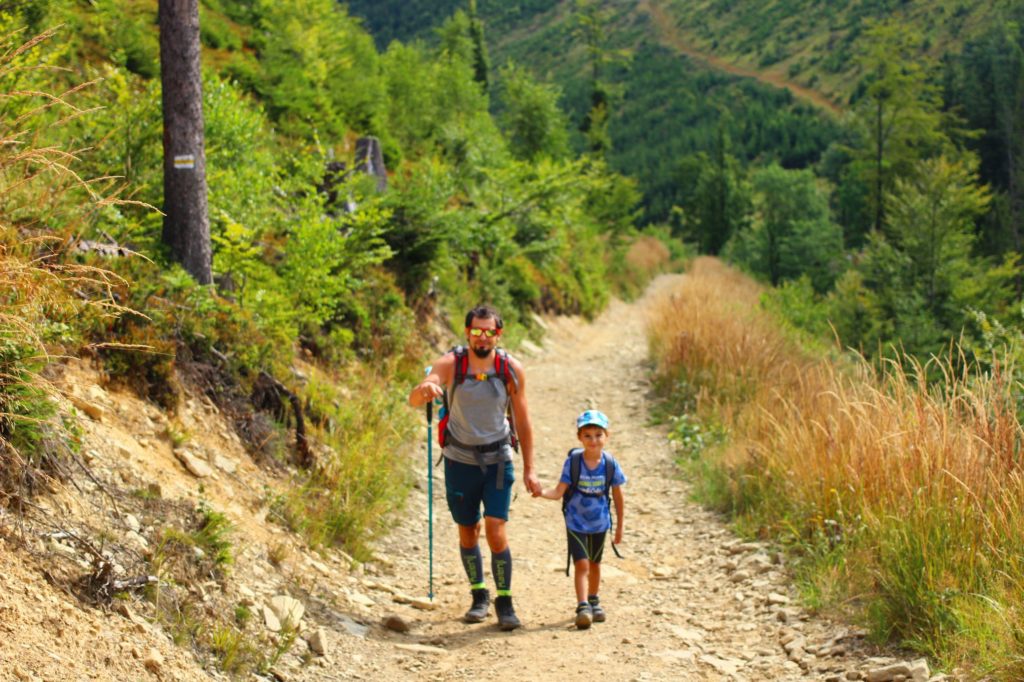 Mężczyzna idący z dzieckiem, utwardzoną, kamienistą drogą, żółtym szlakiem na Wielką Raczę