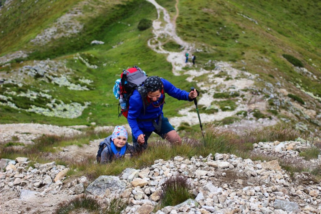 Uśmiechnięty mężczyzna z dzieckiem pokonujący kamieniste podejście na szczyt Brestowa szlakiem niebieskim