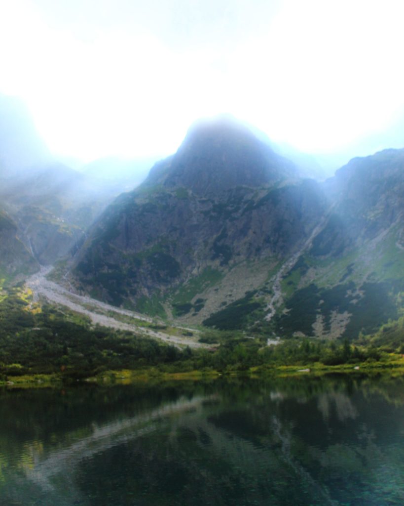 Widok na Tatry Wysokie z nad Zielonego Stawu Kieżmarskie odbijające się w tafli wody, promienie słoneczne oświetlają szczyty