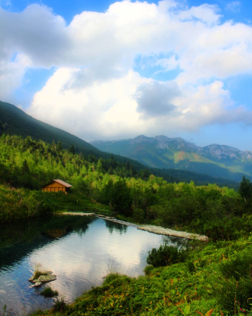 Widok na Zielony Potok oraz tatrzańskie szczyty z końcówki żółtego szlaku nad Zielony Staw Kieżmarski, niebieskie niebo oraz białe chmury odbijające się w tafli wody