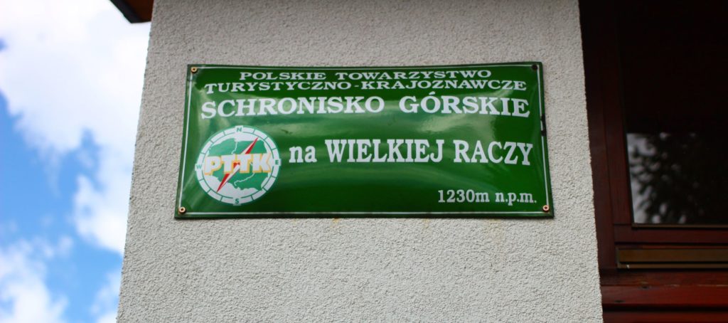 Zielona tabliczka informująca - Schronisko Górskie na Wielkiej Raczy 1230 metrów nad poziomem morza oznaczenie PTTK