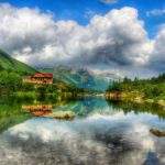 Zielony Staw Kieżmarski - w tle chata przy zielonym stawie, w tle szczyty Tatr Wysokich, niebo z białymi, gęstymi chmurami odbijające się w zielonym stawie