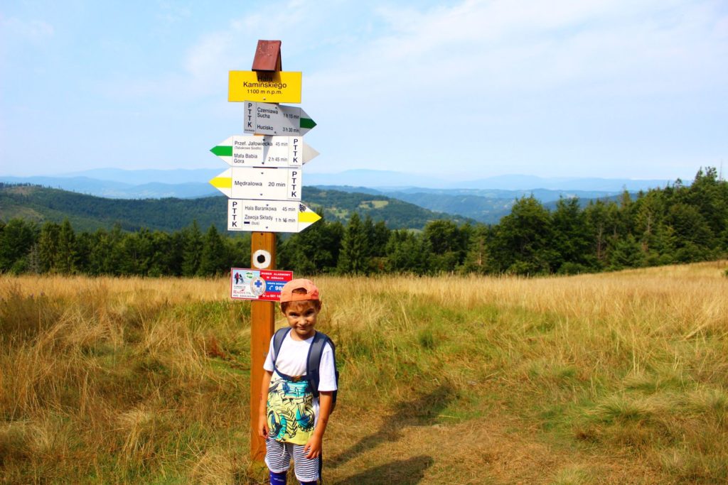 dziecko stojące przy słupie oznaczającym Halę Kamińskiego, w tle polana oraz krajobrazy górskie