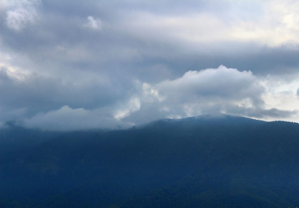 Babia Góra w chmurach widziana z czarnego szlaku prowadzącego na Halę Kamińskiego na tle zachmurzonego nieba