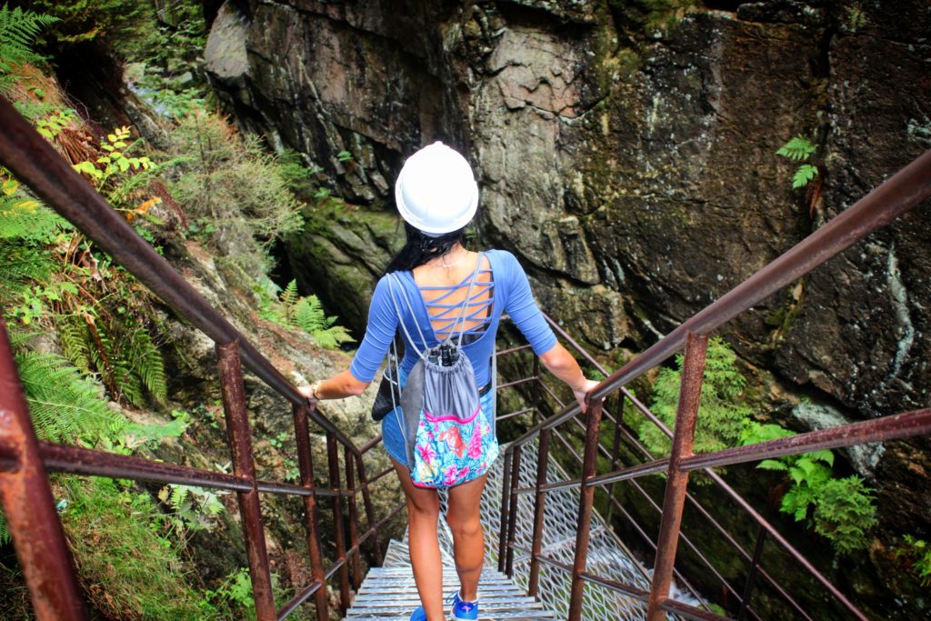 Kobieta w kasku Karkonoskiego Parku Narodowego schodząca po stromych, metalowych schodach, w koło skalne ściany, droga prowadząca do Wodospadu Kamieńczyk