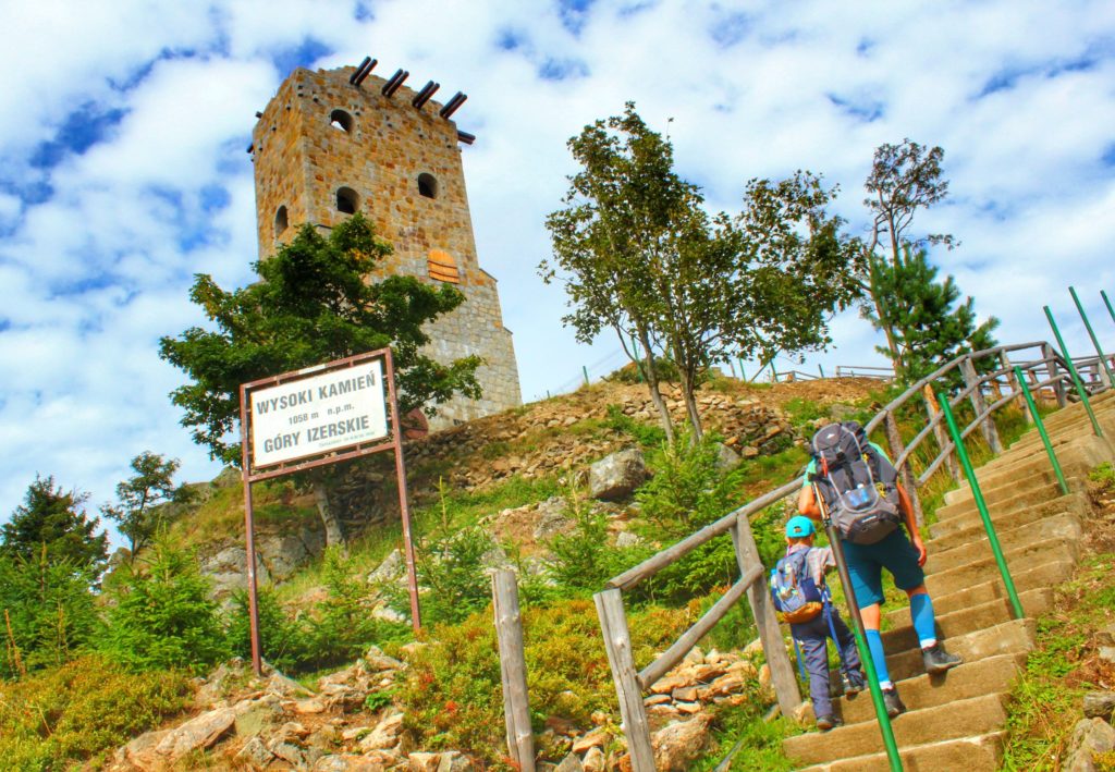 Turysta z dzieckiem wychodzący po schodach prowadzących do schroniska Wysoki Kamień, w tle kamienna wieża widokowa